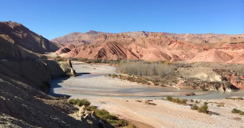 Dry riverbed beneath red striped hills