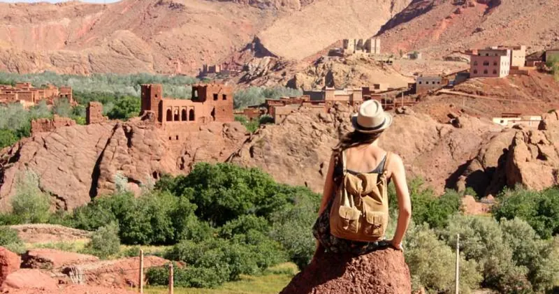Traveller in a hat looking out over a kasbah and an oasis